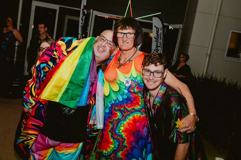 Rainbow united members wearing colourful clothes and hugging, smiling at the camera
